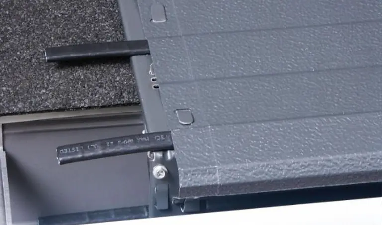 Close-up of gray gutter cover with black heating cables over dark shingles